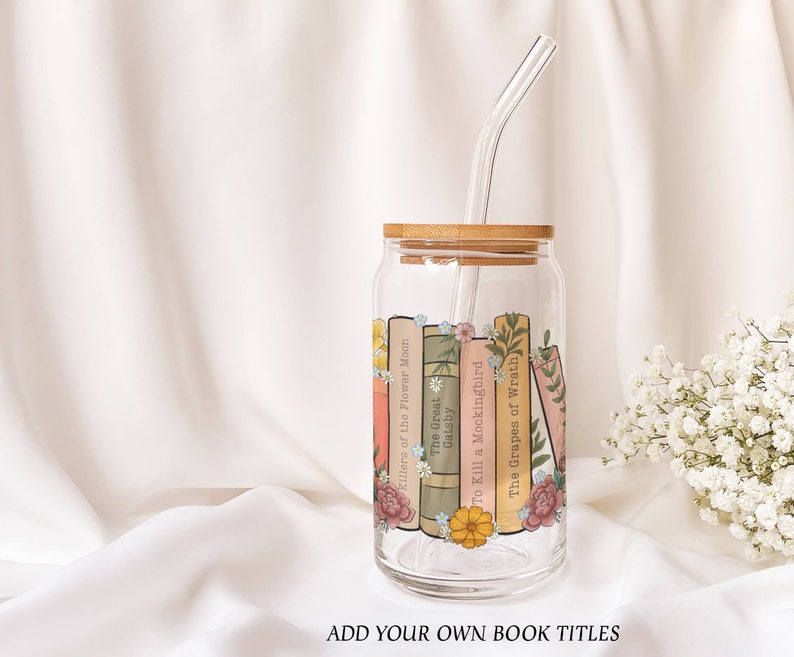 Puede incluir: Un vaso de vidrio transparente con tapa de bamb&uacute; y una pajita. El vaso est&aacute; decorado con un dise&ntilde;o de libros y flores. Los t&iacute;tulos de los libros incluyen "Killers of the Flower Moon", "The Great Gatsby", "To Kill a Mockingbird" y "The Grapes of Wrath".