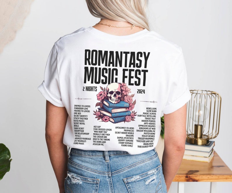 May include: White t-shirt featuring the text "ROMANTASY MUSIC FEST 2024" with a skull and floral design. The back of the shirt lists various romance novel tropes. A unique graphic tee for book lovers.