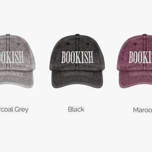 May include: Three baseball caps in charcoal grey, black, and maroon. Each cap has the word "BOOKISH" embroidered in white across the front. The caps are displayed against a white background.