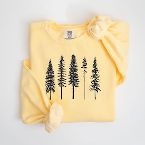 May include: A yellow sweatshirt with a black silhouette of five pine trees printed on the front. The sweatshirt is folded in half and the sleeve is rolled up.