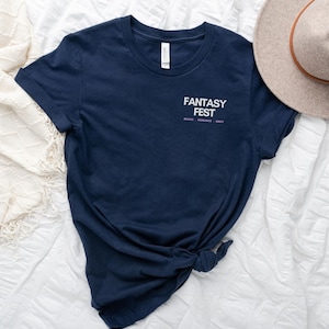 May include: A navy blue t-shirt with the text "Fantasy Fest" in white with the words "Magic, Romance, Smut" in smaller purple text below.