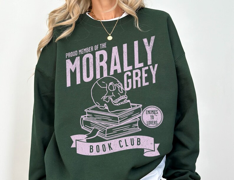 Puede incluir: Una sudadera verde oscuro con un estampado gr&aacute;fico rosa que dice "Proud Member of the Morally Grey Book Club". El gr&aacute;fico tambi&eacute;n incluye una calavera, libros y el texto "Enemies to Lovers".