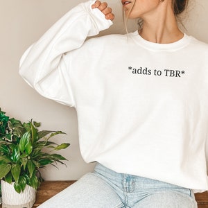 May include: White sweatshirt with the text "*adds to TBR*" printed on the front.