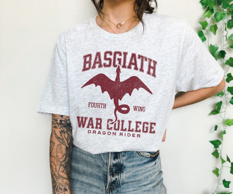 May include: A grey t-shirt with a red dragon graphic and the text "Basgiath Fourth Wing War College Dragon Rider".