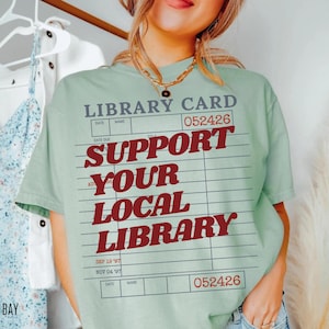 Woman wearing oversized bay green t shirt with vintage library card graphic and support your local library text styled indoors