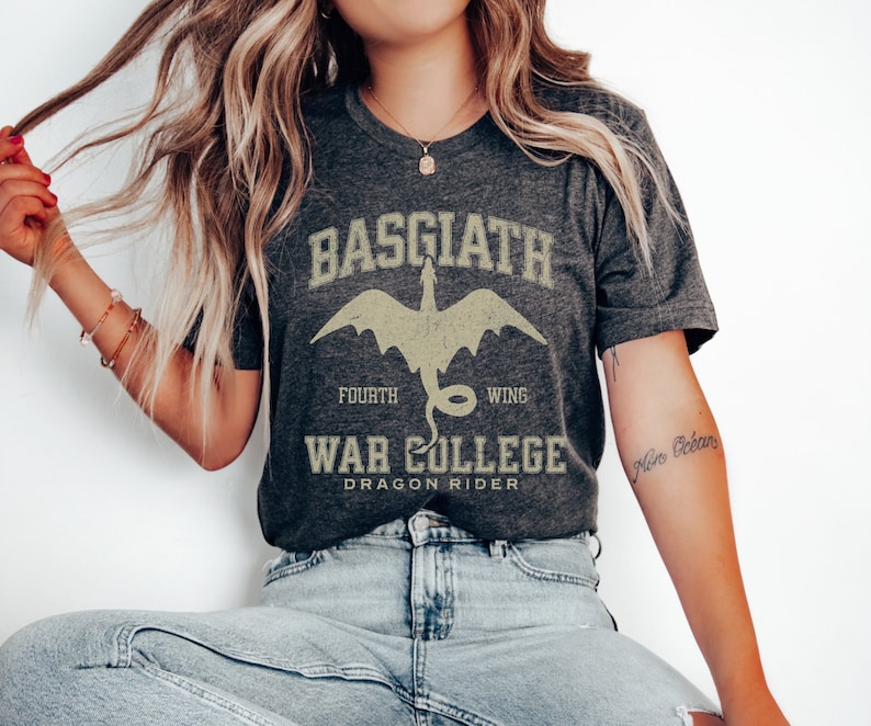 May include: A dark grey t-shirt with a graphic print of a dragon and the text "Basgiath Fourth Wing War College Dragon Rider".