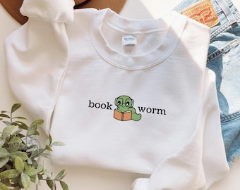 May include: White crewneck sweatshirt with the words "book worm" and a cartoon worm wearing glasses and reading a book. The worm is green, the book is orange, and the text is black.