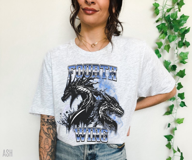 K&ouml;nnte beinhalten: Ein graues T-Shirt mit einem schwarzen und blauen Grafikdruck von drei Drachen mit dem Text "FOURTH WING" auf der Vorderseite.
