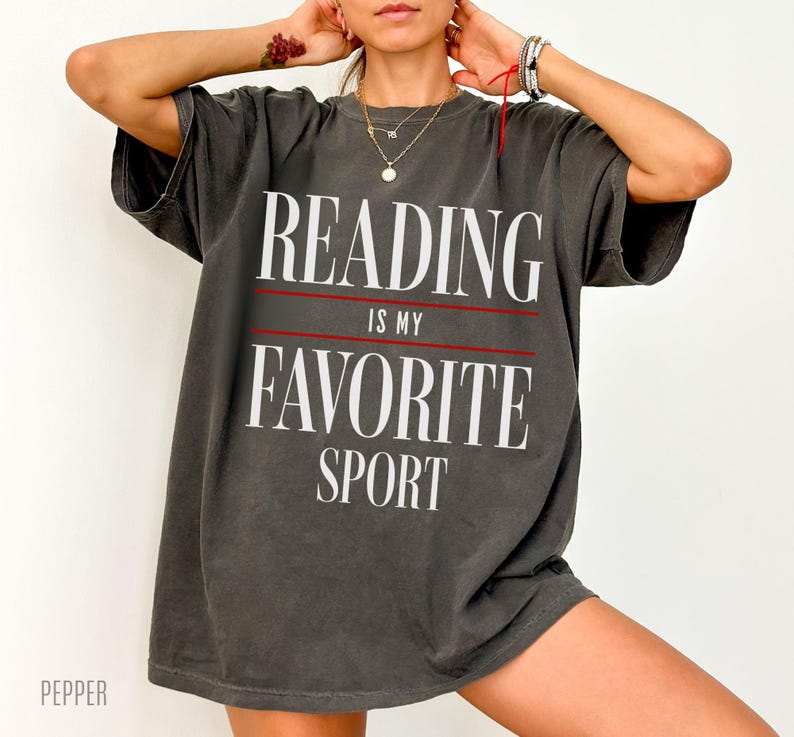 May include: A dark gray oversized t-shirt with the text "Reading is my favorite sport" printed in white on the front.