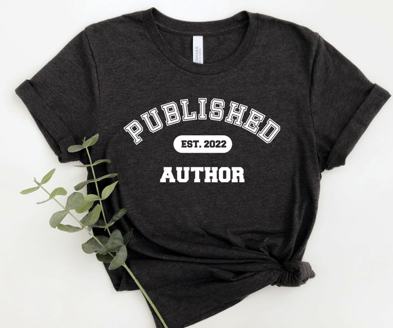 May include: A dark gray t-shirt with white text that reads "PUBLISHED EST. 2022 AUTHOR".