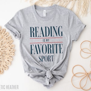 Może przedstawiać: Szara koszulka z nadrukiem "Reading is my favorite sport" w kolorze granatowym i czerwonym.