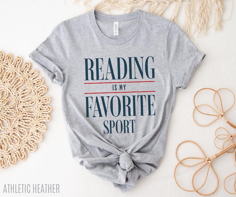 Może przedstawiać: Szara koszulka z nadrukiem "Reading is my favorite sport" w kolorze granatowym i czerwonym.
