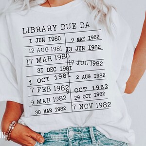 May include: White t-shirt with black text that reads "LIBRARY DUE DA" and a list of dates from 1980 to 1982.
