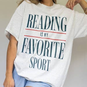 May include: A gray t-shirt with the text "Reading is my favorite sport" printed in blue and red.