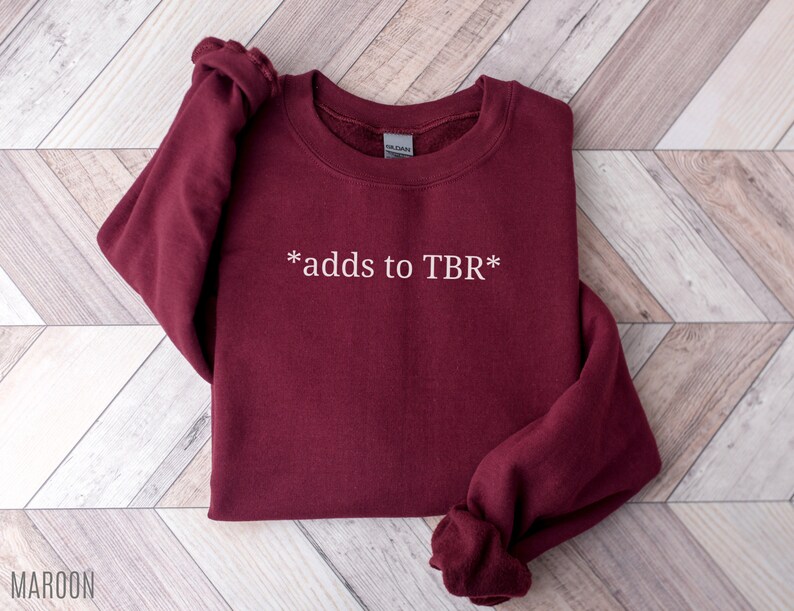 May include: Maroon sweatshirt with the text "*adds to TBR*" in white.