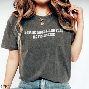 May include: A dark gray t-shirt with the text "Buy me books and tell me I'm pretty" in white letters.