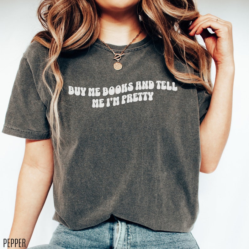 May include: A dark gray t-shirt with the text "Buy me books and tell me I'm pretty" in white letters.