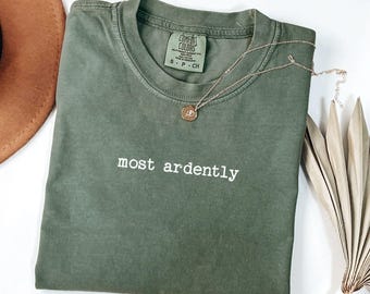 Op de afbeelding: Een mosgroen t-shirt met de tekst "most ardently" in wit gedrukt. Het shirt heeft een label met de tekst "Comfort Colors" en een maatlabel met de tekst "S - P - CH".