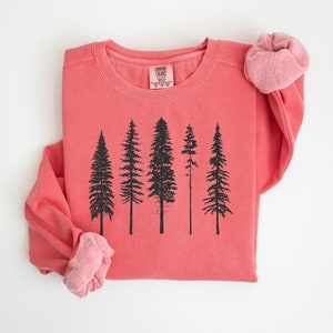 May include: A coral colored sweatshirt with a black silhouette of five pine trees printed on the front. The sweatshirt has a crew neck and long sleeves.