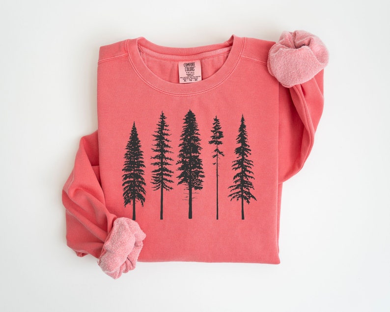May include: A coral colored sweatshirt with a black silhouette of five pine trees printed on the front. The sweatshirt has a crew neck and long sleeves.