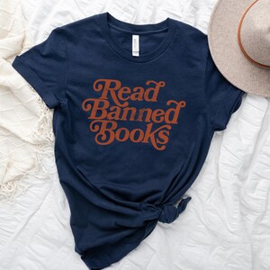 May include: Navy blue t-shirt with the text "Read Banned Books" in a retro orange font.