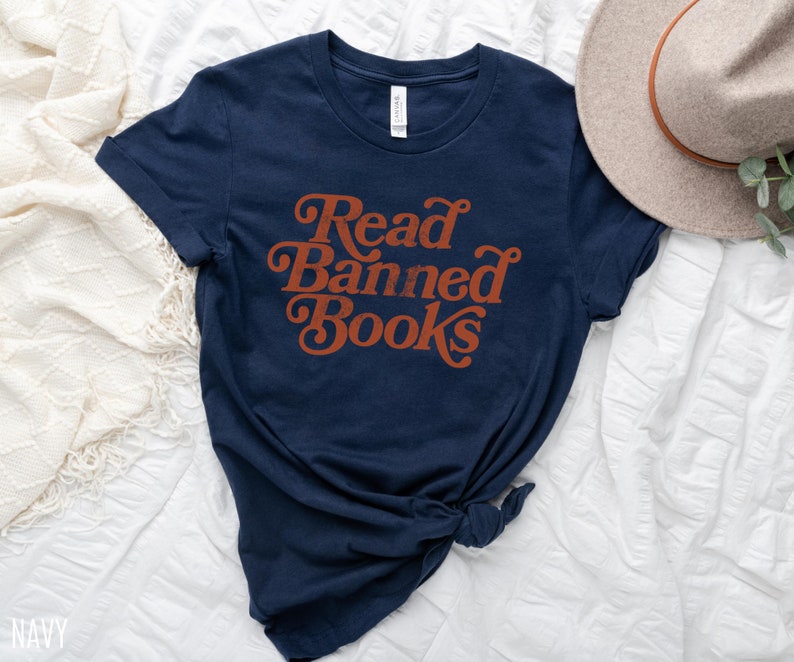 May include: Navy blue t-shirt with the text "Read Banned Books" in a retro orange font.