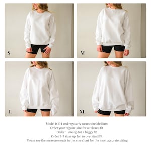 May include: Four images displaying a white crewneck sweatshirt in sizes S, M, L, and XL. Each image shows a person wearing the sweatshirt with black shorts. Text at the bottom advises on sizing: order regular size for relaxed fit, one size up for baggy, and two to three sizes up for oversized.