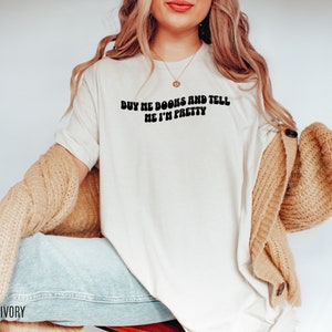 May include: A white t-shirt with the text "Buy me books and tell me I'm pretty" in black, retro-style lettering.