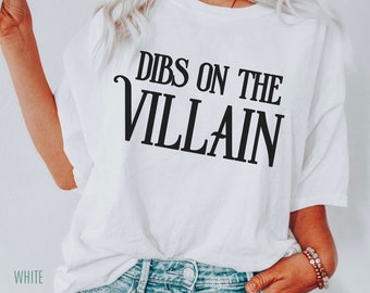 Könnte beinhalten: Ein weißes kurzärmeliges T-Shirt mit dem schwarzen Schriftzug DIBS ON THE VILLAIN, der in einer fetten, stilisierten Schrift auf der Brust gedruckt ist. Das Kleidungsstück hat einen Rundhalsausschnitt und eine lockere Passform.