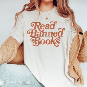 May include: A white t-shirt with the text "Read Banned Books" in a retro orange font.