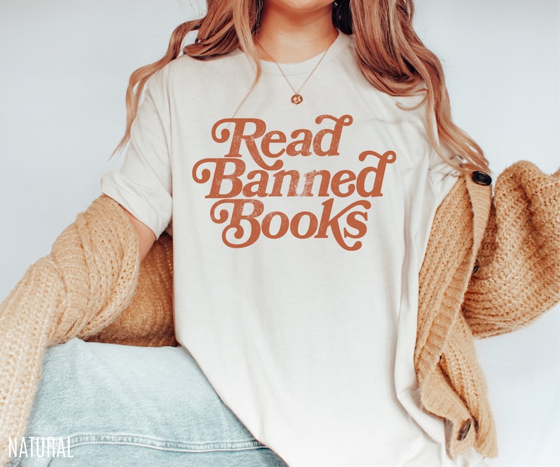 May include: A white t-shirt with the text "Read Banned Books" in a retro orange font.