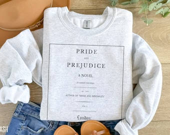 Puede incluir: Una sudadera gris con una impresión negra de la página de título de la novela "Orgullo y Prejuicio" de Jane Austen. El texto dice "Orgullo y Prejuicio, Una novela, en tres volúmenes, por la autora de "Sentido y Sensibilidad", Vol. I, Londres."