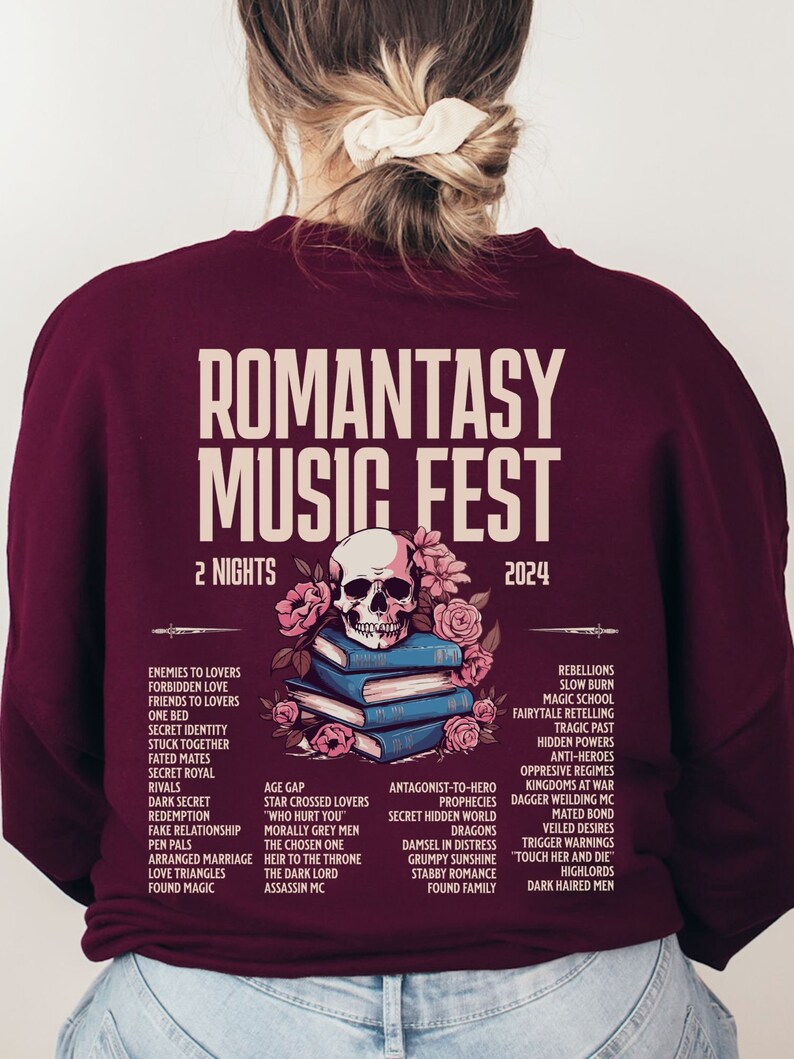 May include: A burgundy sweatshirt featuring "ROMANTASY MUSIC FEST 2024" text. The design includes a skull and flowers over books. The back lists romance novel themes and tropes, with "2 NIGHTS" displayed.