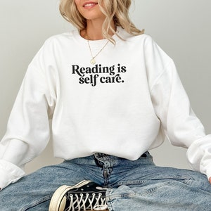 May include: White sweatshirt with the text "Reading is self care." printed in black.