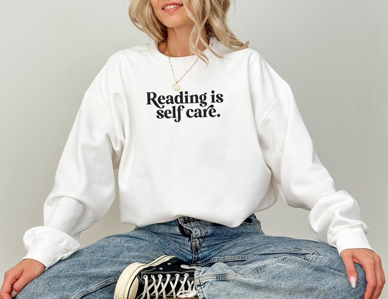 May include: White sweatshirt with the text "Reading is self care." printed in black.