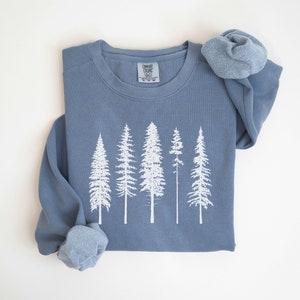May include: A blue sweatshirt with a white print of five pine trees. The sweatshirt is folded and the sleeves are rolled up.