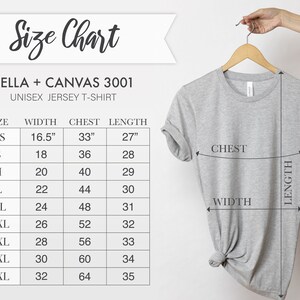 Puede incluir: Una camiseta unisex Bella + Canvas 3001 gris claro colgada de una percha de madera. La imagen incluye una tabla de tallas con medidas en cm para ancho, pecho y largo, desde XS hasta 5XL.