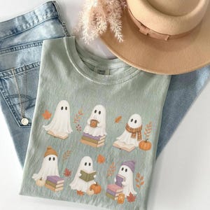 Bay Comfort Colors shirt featuring six cute Halloween ghosts reading and sitting on books, surrounded by pumpkins, autumn leaves, and cozy fall accessories.