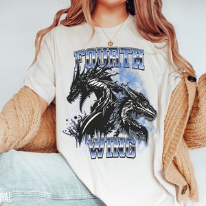 K&ouml;nnte beinhalten: Ein wei&szlig;es T-Shirt mit einem Aufdruck von zwei schwarzen Drachen und dem Text "FOURTH WING" in blauer Schrift.