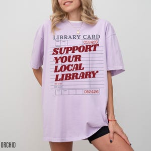 Woman wearing oversized orchid purple t shirt with vintage library card graphic and support your local library text styled casually