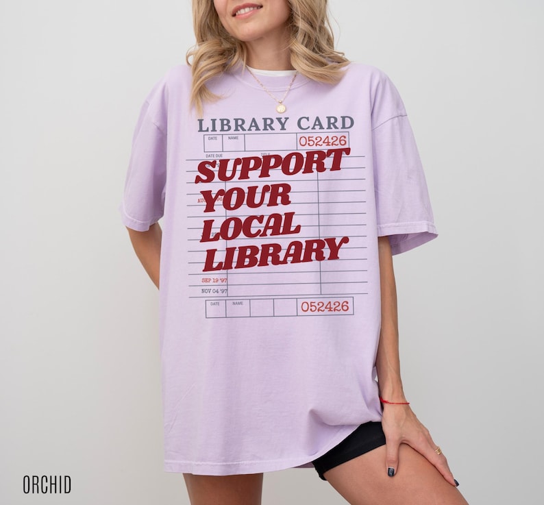 Woman wearing oversized orchid purple t shirt with vintage library card graphic and support your local library text styled casually