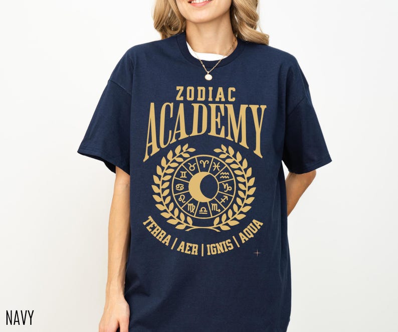 May include: Navy blue t-shirt with a gold graphic design. The design features the words "ZODIAC ACADEMY" above a circular emblem with zodiac symbols, a crescent moon, and the words "TERRA | AER | IGNIS | AQUA".