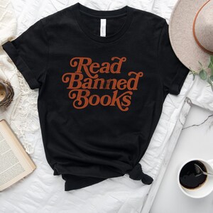 May include: Black t-shirt with the text "Read Banned Books" in orange retro font.