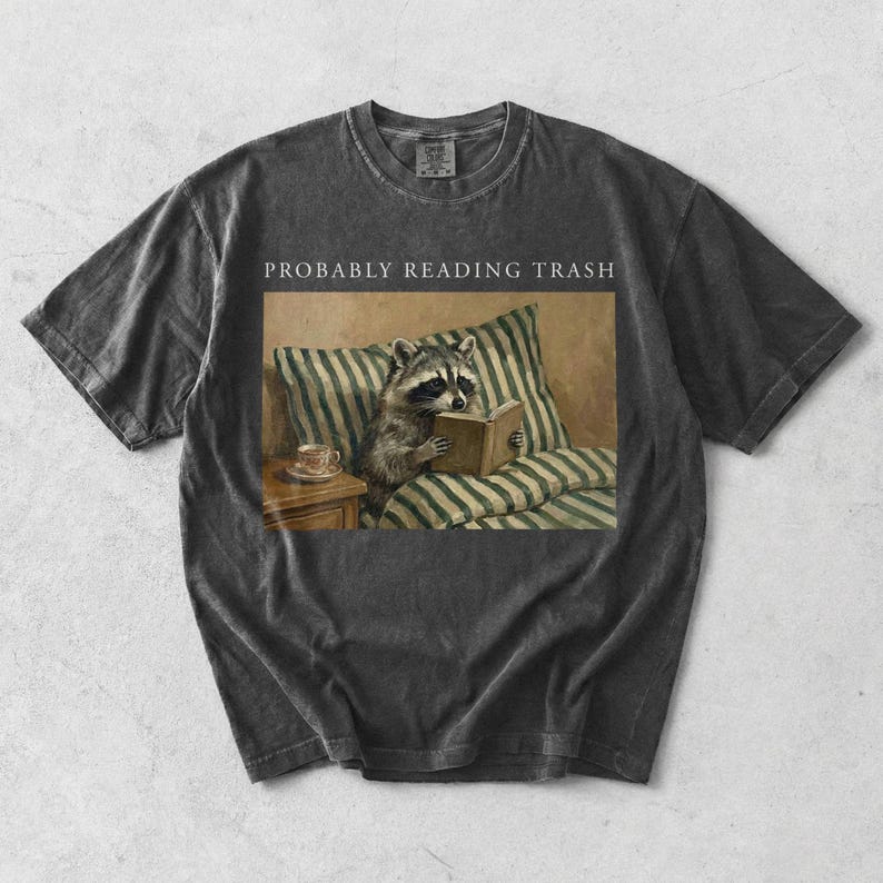 Pepper Comfort Colors t shirt laid flat with probably reading trash text and raccoon reading book vintage illustration