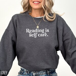 May include: Heather grey sweatshirt with the text "Reading is self care." in white.