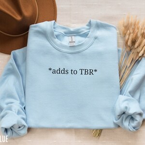 May include: Light blue sweatshirt with the text "*adds to TBR*" printed on the front.