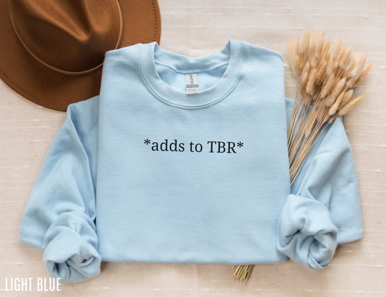 May include: Light blue sweatshirt with the text "*adds to TBR*" printed on the front.