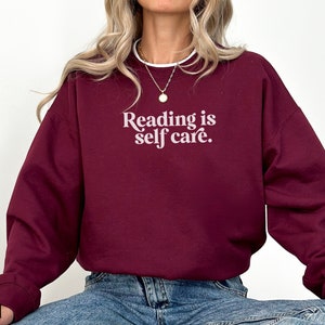 May include: A maroon sweatshirt with the text "Reading is self care." in white.