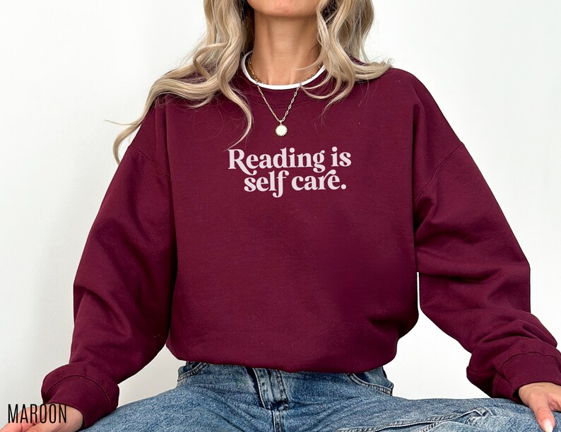 May include: A maroon sweatshirt with the text "Reading is self care." in white.