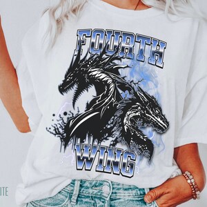 K&ouml;nnte beinhalten: Wei&szlig;es T-Shirt mit einer schwarzen und wei&szlig;en Grafik von zwei Drachen und dem Text "FOURTH WING" in blauen und silbernen Buchstaben.